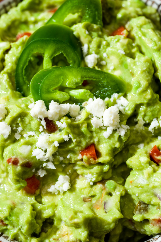 Close-up of sliced jalepenos with queso freso in pimento guacamole with round yellow corn tortilla chip.