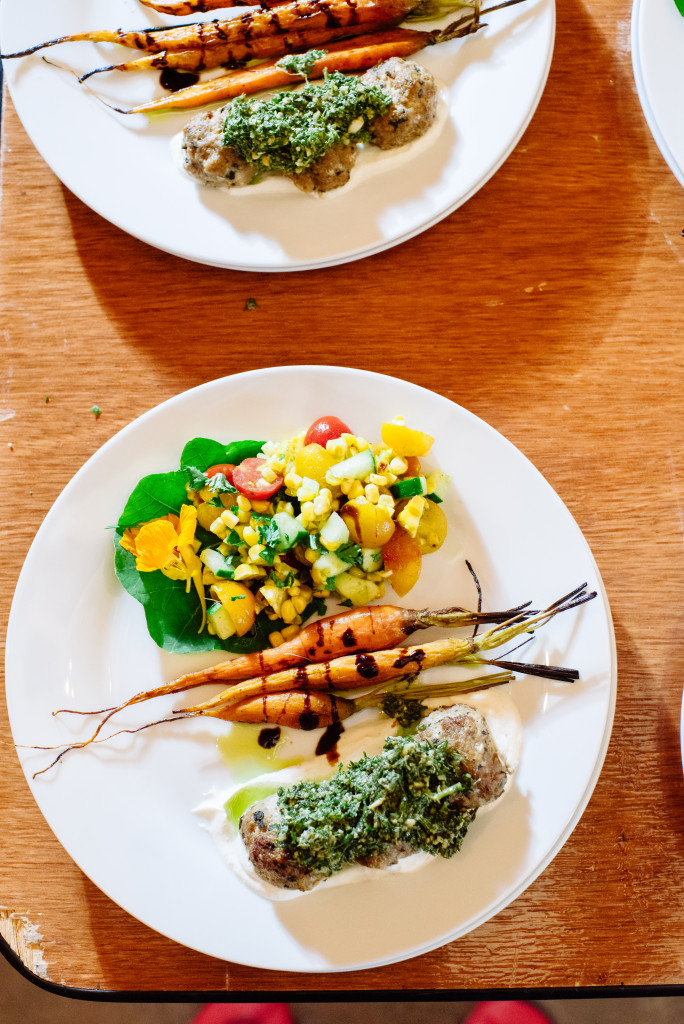 Overhead of white plate with roasted carrots and balsamic drizzle with lamb meatballs and greens pesto and corn salad.